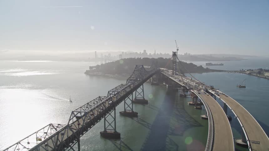 Aerial view of a bridge over water with vehicles and a city skyline in the distance