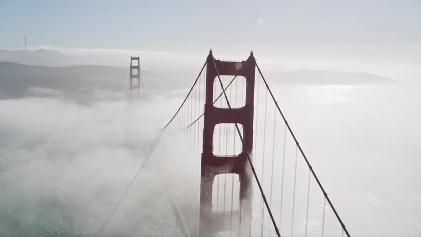 Heavy fog flows over the golden gate bridge while multiple boats leave wakes through the ocean