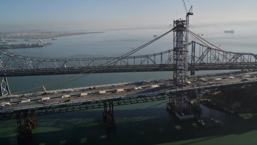 Aerial panorama of a bridge with vehicle traffic and next to it a bridge being built with a metropolis on the horizon