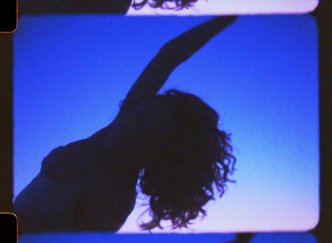 Silhouette of a woman dancing against a blue and red sky near the beach