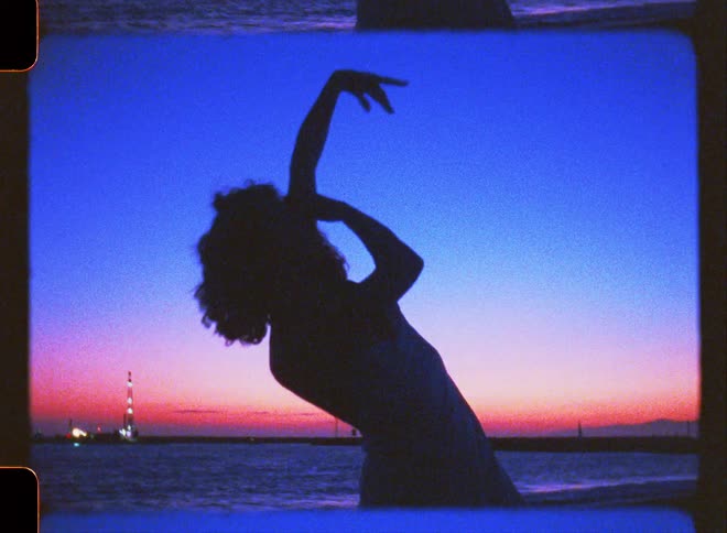 Silhouette of a woman on the beach dancing while there is a blue and red sky on the horizon