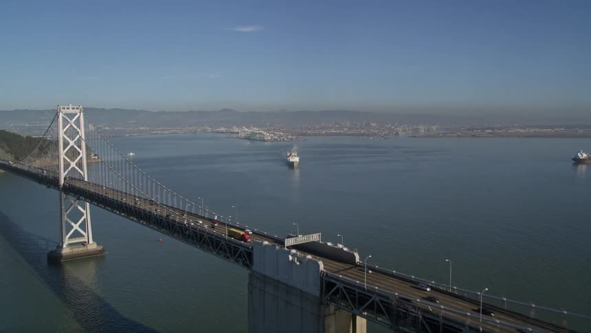 Aerial panorama of a long bridge over the sea with a cargo ship traveling