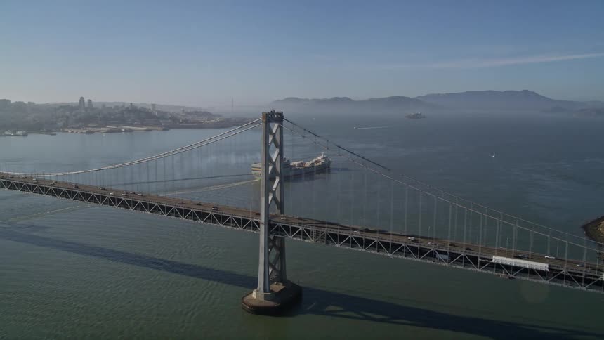Aerial panorama of a doubledecker sea bridge with vehicle traffic and a cargo ship passing by