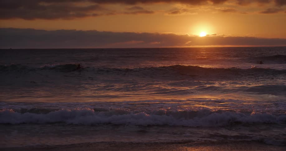 Two surfers in the sea at sunset letting the waves pass