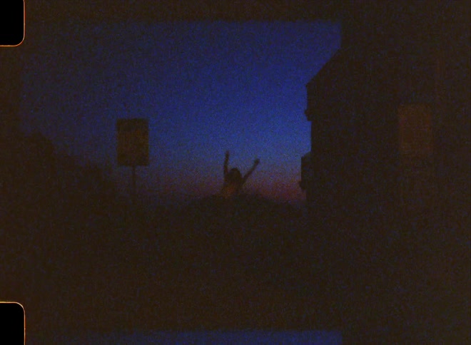 Silhouette of a woman dancing in a dark outdoor environment with the blue and orange sky on the horizon