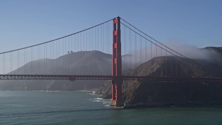 Aerial panorama of a red bridge over the sea and next to the rocky coast during the day