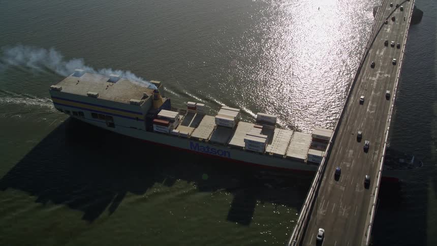 Aerial panorama of a cargo ship crossing under a bridge towards a metropolis