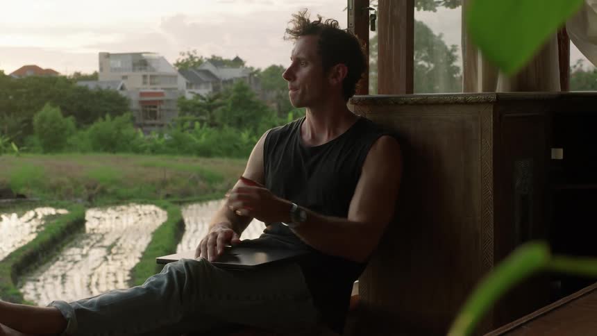 Sitting outside a man closes his laptop and rests his arms on top of it