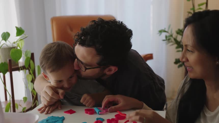 Father giving his son a kiss and his mother next to him smiling as they play with modeling clay