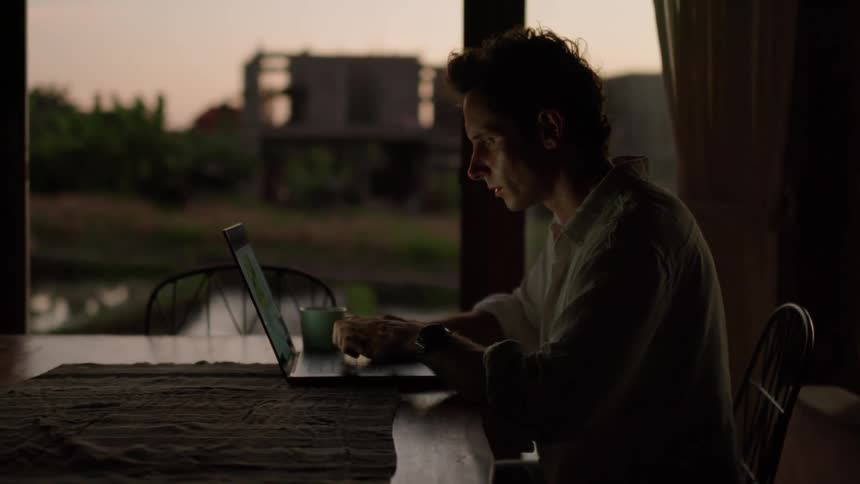 Side portrait of a man sitting at a desk typing on his laptop
