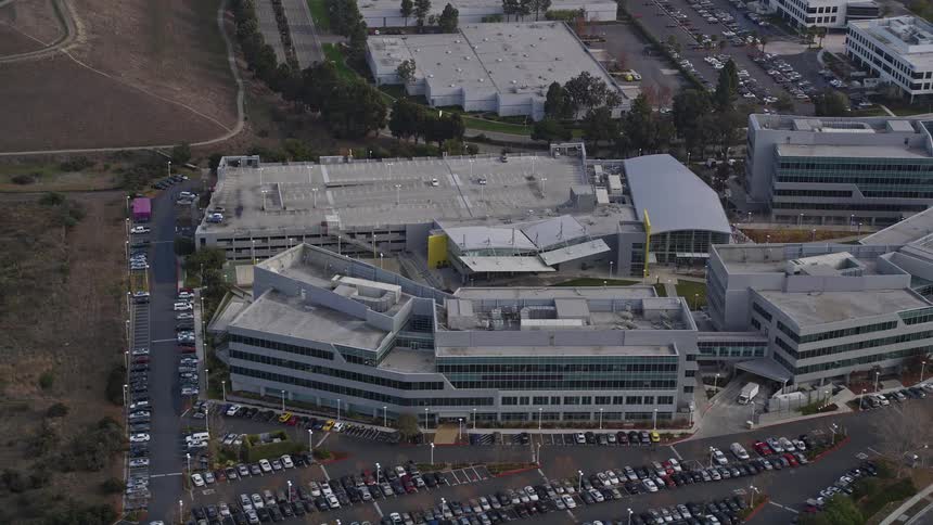 A cluster of a few identical buildings with a large parking lot in front and an empty field to the side