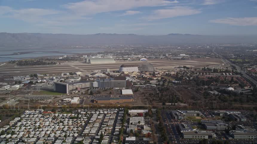 This aerial view showcases a city sprawling alongside a runway and various buildings of moffett federal airfield in california