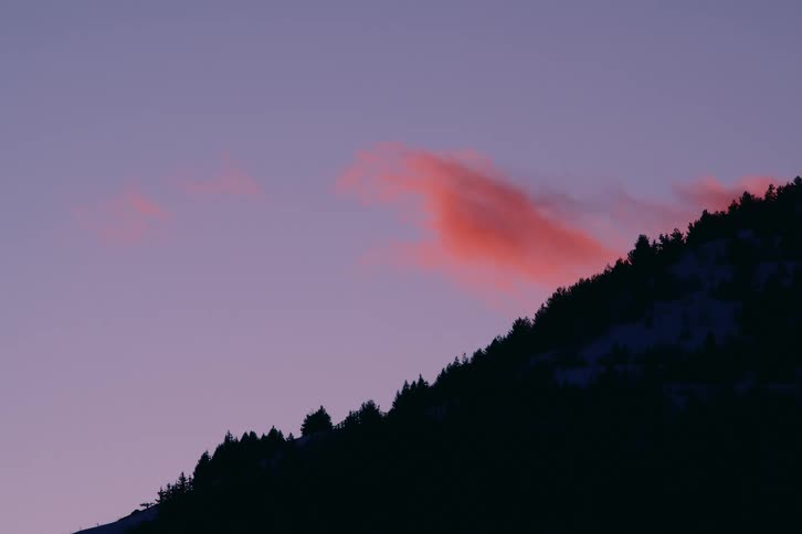 Silhouette of a mountain ridge against a twilight sky with pink clouds