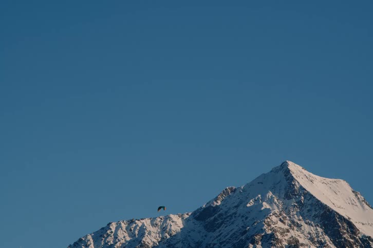 A parachutist landing next to a huge snowcovered mountain in contrast to a clear blue sky
