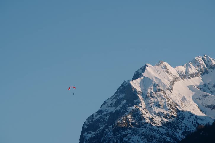 Upward view of a snowcovered mountain and a person with a parachute