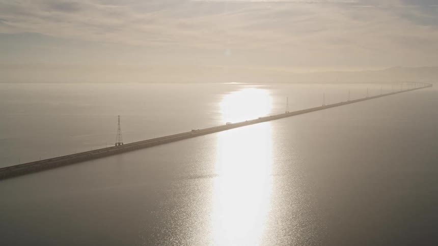 Aerial panorama of an extensive highway over the sea with vehicle traffic and the reflection of the sun on the horizon