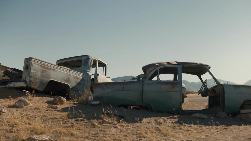 Two broken down cars are laying in the desert