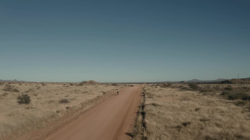 Person riding a bicycle on a dirt road in the middle of a desert biome natural environment on a cloudless blue sky day
