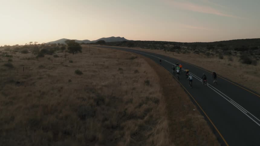 A group of cyclists together on an asphalt street with empty fields on the sides