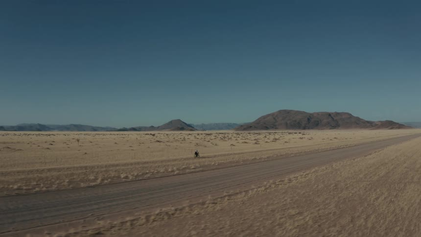 Landscape of a person riding a bicycle in a natural desert environment with mountains on the horizon on a cloudless blue sky day