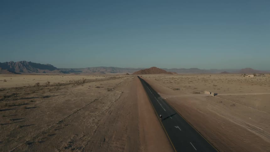 A straight road cuts through a barren desert landscape under a clear sky