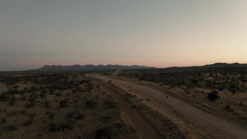 A cyclist on a dirt street in a desert region with mountains in the background