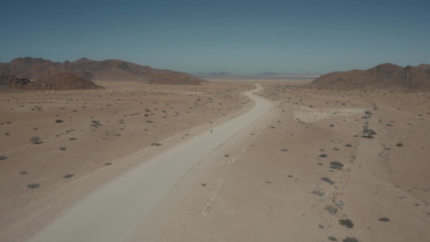 Aerial panorama of a desert scenery with a dirt road with cyclist pedaling and a clear blue sky