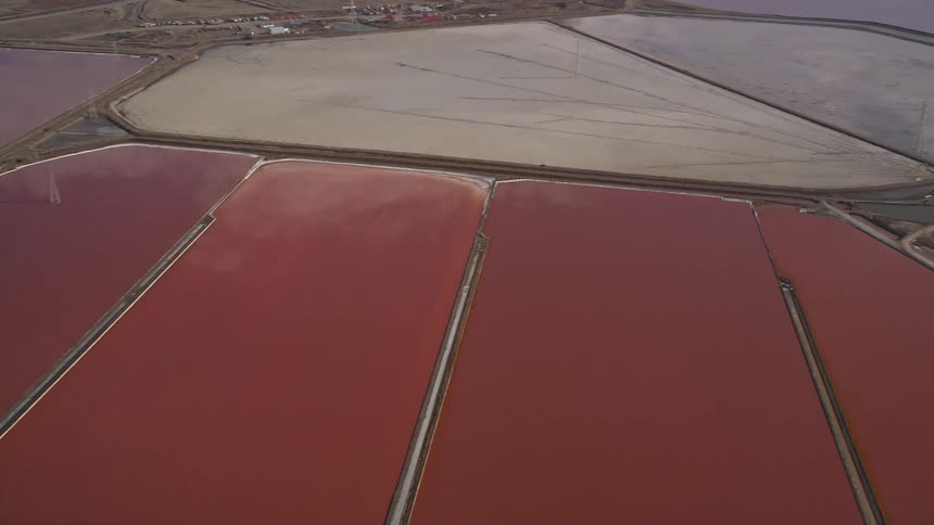Aerial view of salt evaporation ponds with reddishpink water separated by narrow pathways