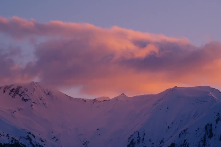 A mountain covered in snow and the sky above is with an orange cloud