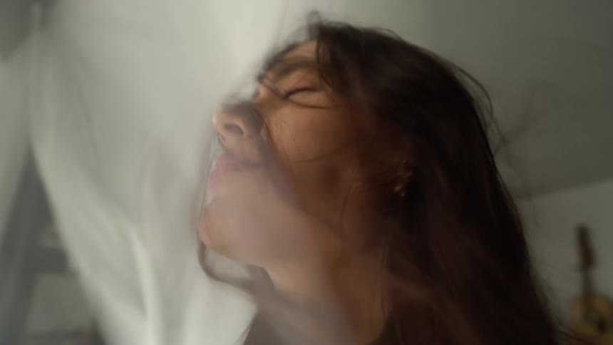 A smiling girl gets her face battered by a blowing curtain