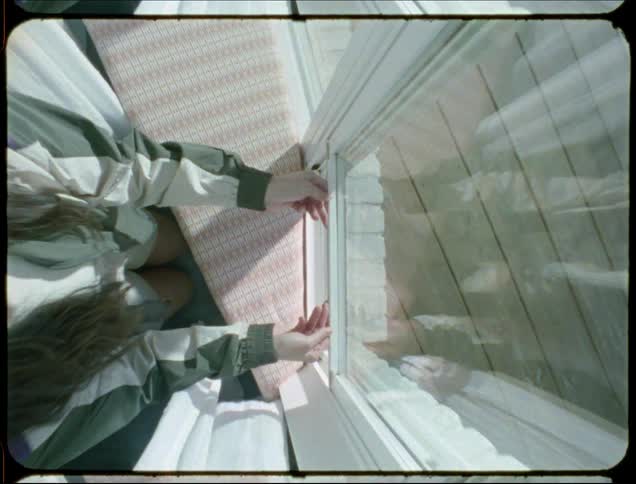 A woman with long hair is seen from an overhead angle opening a window