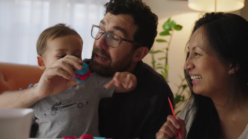 A family laughs as they play with their toddler son