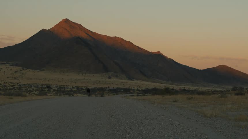 Silhouette of a cyclist cycling on a dirt road in a natural environment with mountains around on a morning
