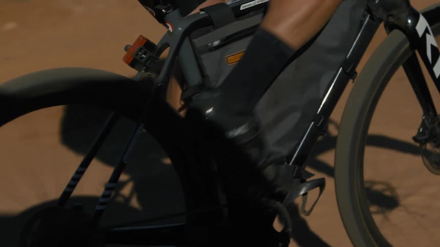A cyclist with glasses a helmet a white jersey black shorts socks and shoes rides a bicycle on a country road