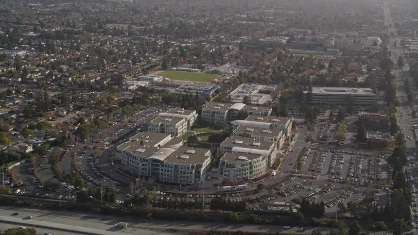A complex of buildings built in a circular shape with parking in front and an avenue with many cars passing by