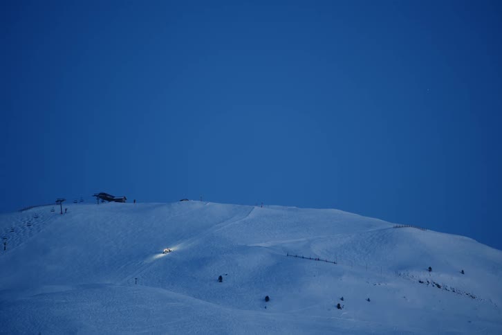 A vehicle driving over a snow covered hill at dusk
