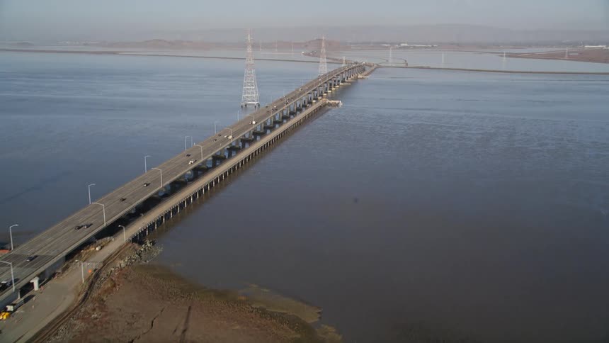 Traffic crosses river bridge passing a pond and multiple open frame towers