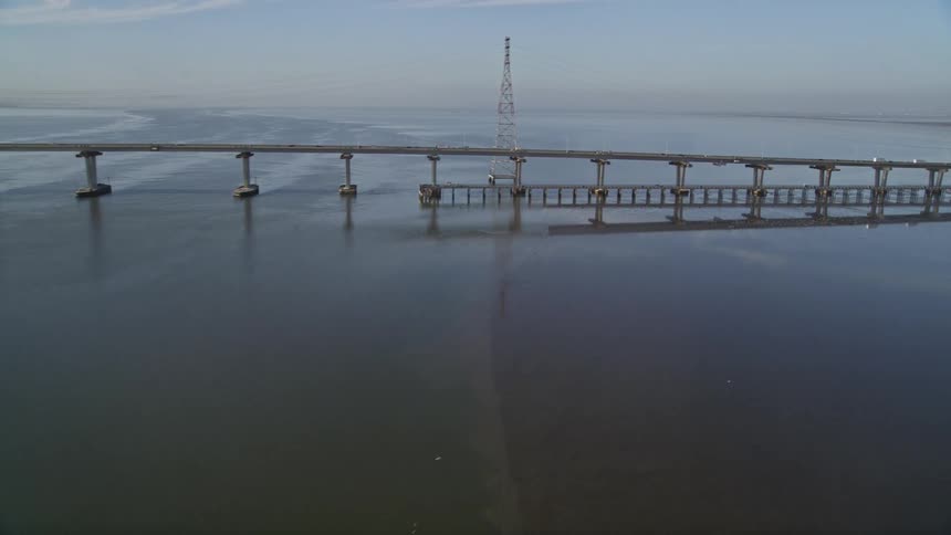Fog shrouds shore in the distance while vehicles cross bridge