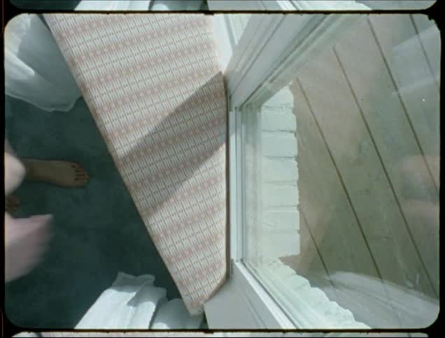 A young woman kneels next to a bay window and shuts it