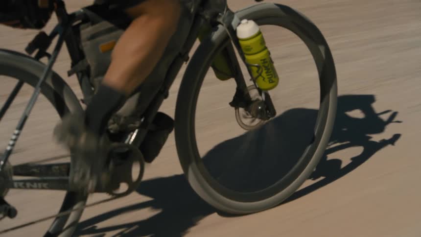 Legs of a male cyclist pedaling on a dirt road with his water bottle in a holder next to the wheel