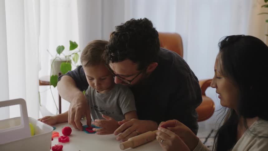 A young child and his parents play with playdough together