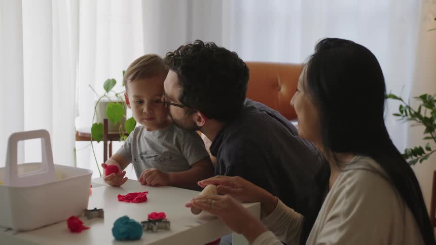 Father giving his son a kiss next to his mother while they play with modeling clay