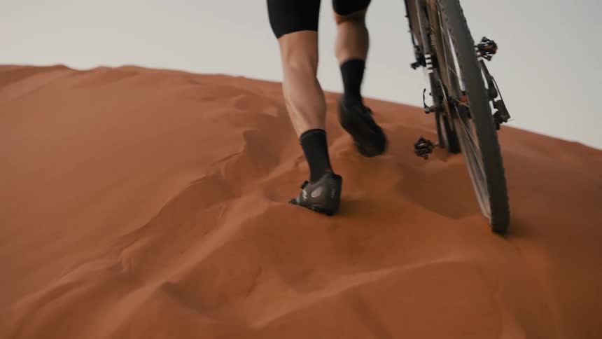 Legs of a man climbing desert dunes with his bicycle
