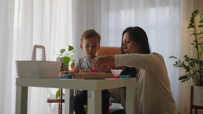 Mother next to her son sitting at a table playing with clay