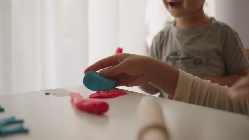 Mother next to her little son playing with modeling clay indoors in the living room