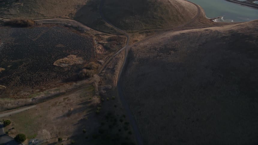 A coast and lots of hills and grasslands surround a rural area