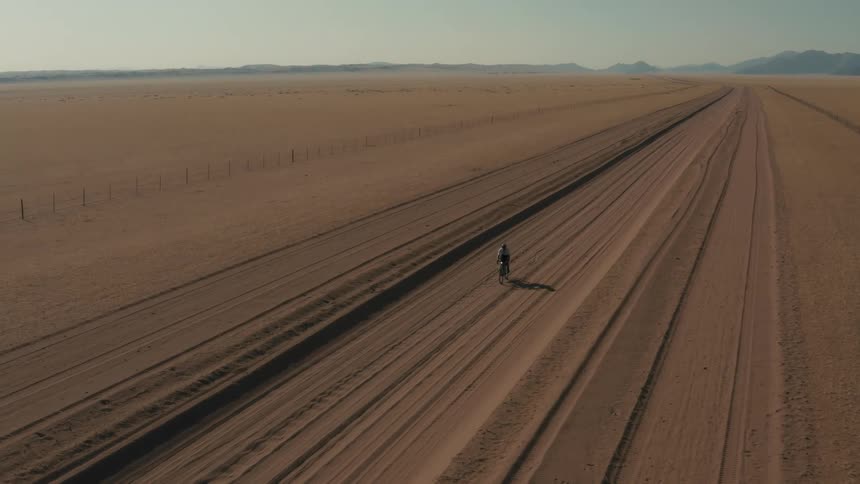 Cyclist wobbles while pedaling along dirt track passing a fenced field