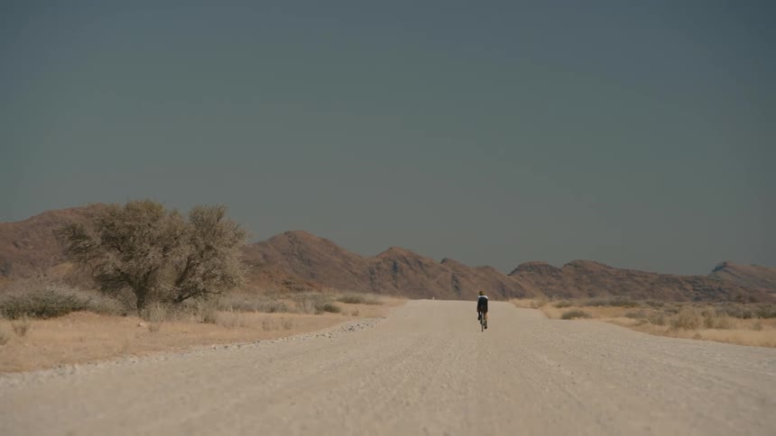 A cyclist is traveling towards a mountain range on a gravel road