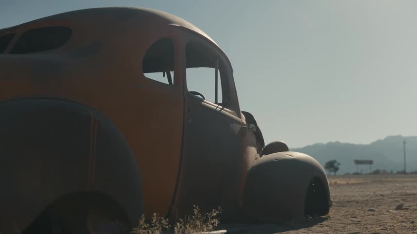 Car without wheels disassembled and rusty in a desert terrain with the silhouette of mountains on the horizon