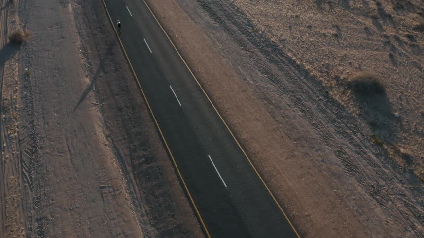 Cyclist riding his bike on a paved street with desert vegetation around on a morning